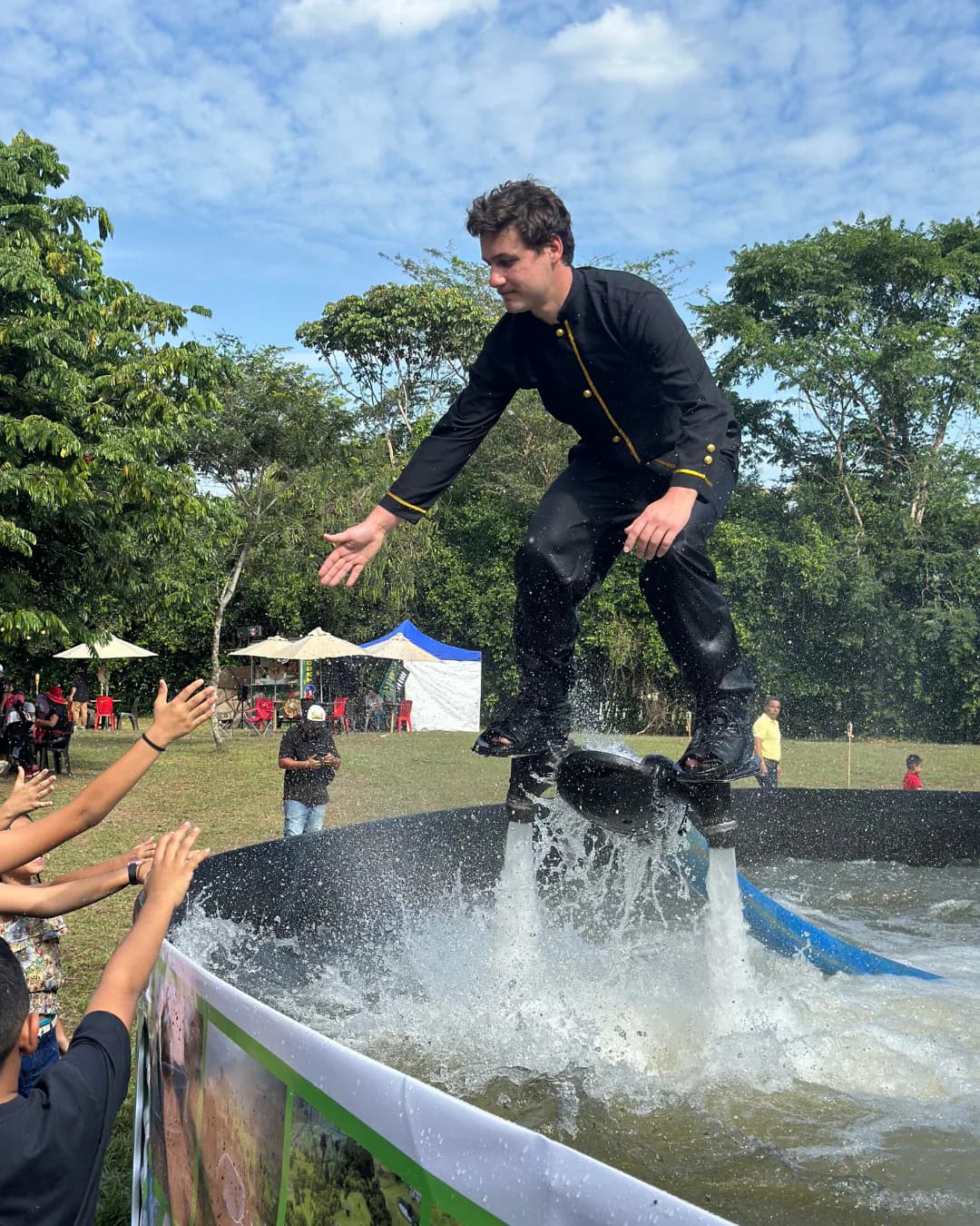 Flyboard performer reaching toward audience members beside an event pool