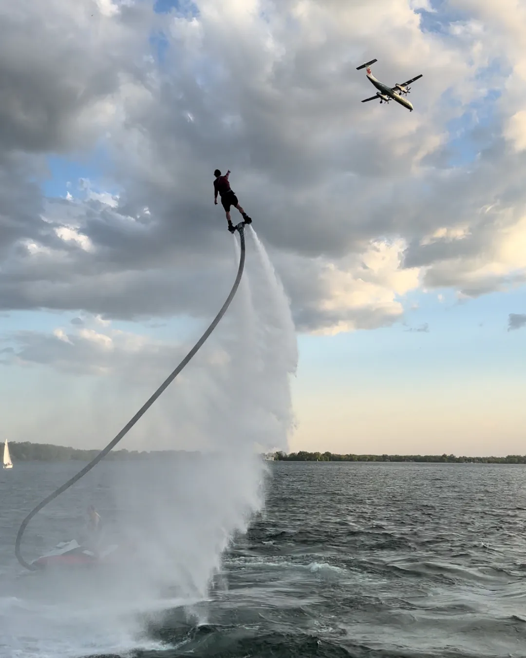 Flyboard rider rising above the water as a passenger aircraft flies overhead