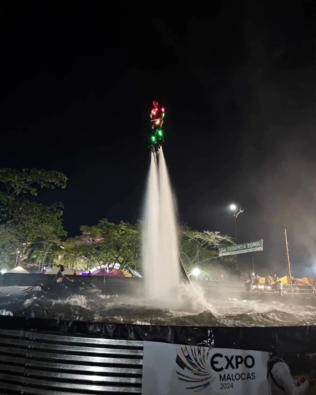 Flyboard performer wearing illuminated red and green equipment during a night show