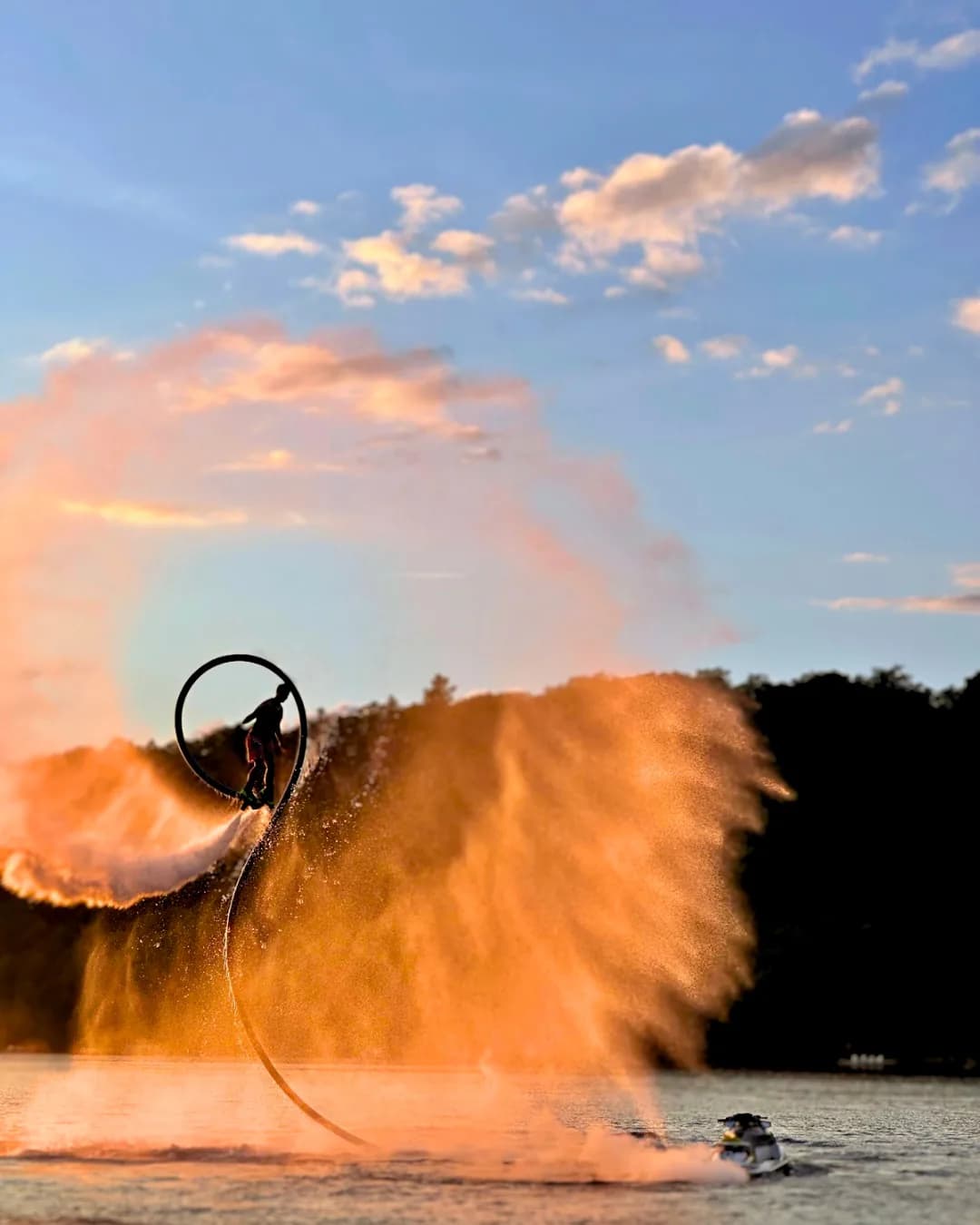 Flyboard performer completing a circular flip through orange sunset spray