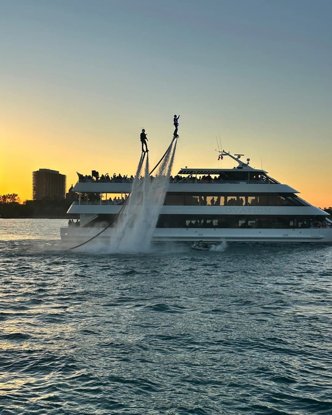 Two Flyboard performers flying beside a passenger yacht at sunset