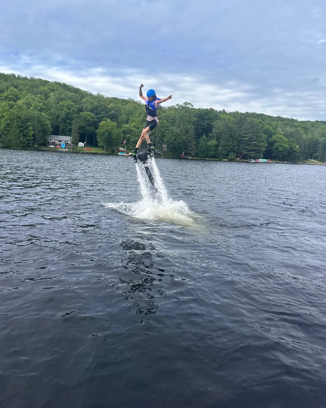 Helmeted beginner balancing on a Flyboard above a tree-lined lake