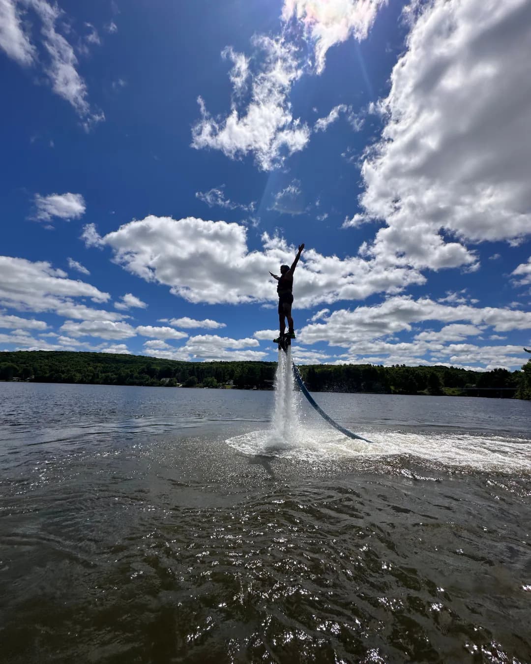 Flyboard rider rising above a cottage lake beneath a dramatic blue sky