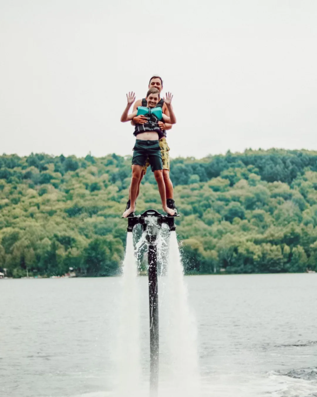 Adult and child riding together on a Flyboard above a lake