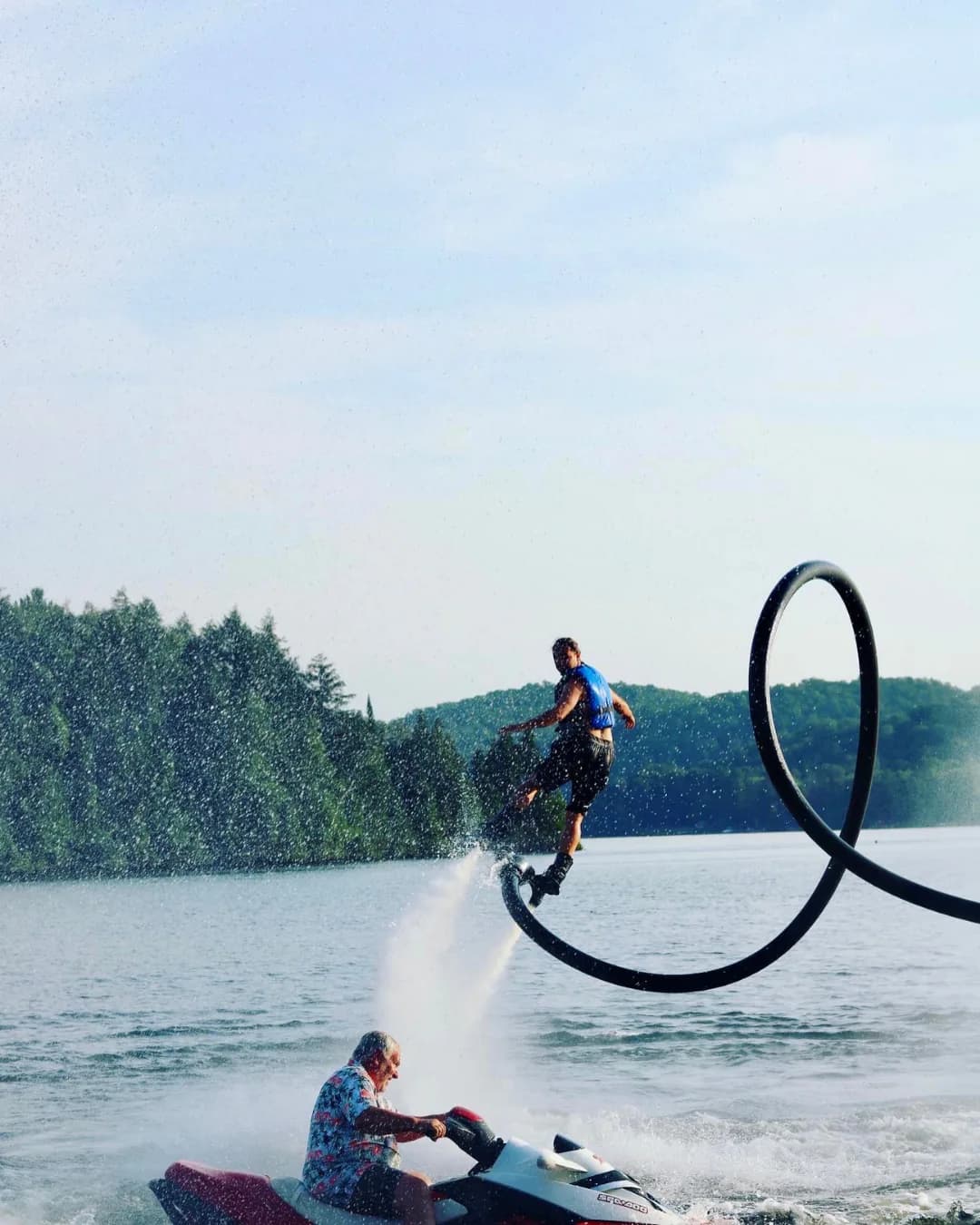 Flyboard rider beside a Sea-Doo on Lake of Bays with a forested shoreline behind him