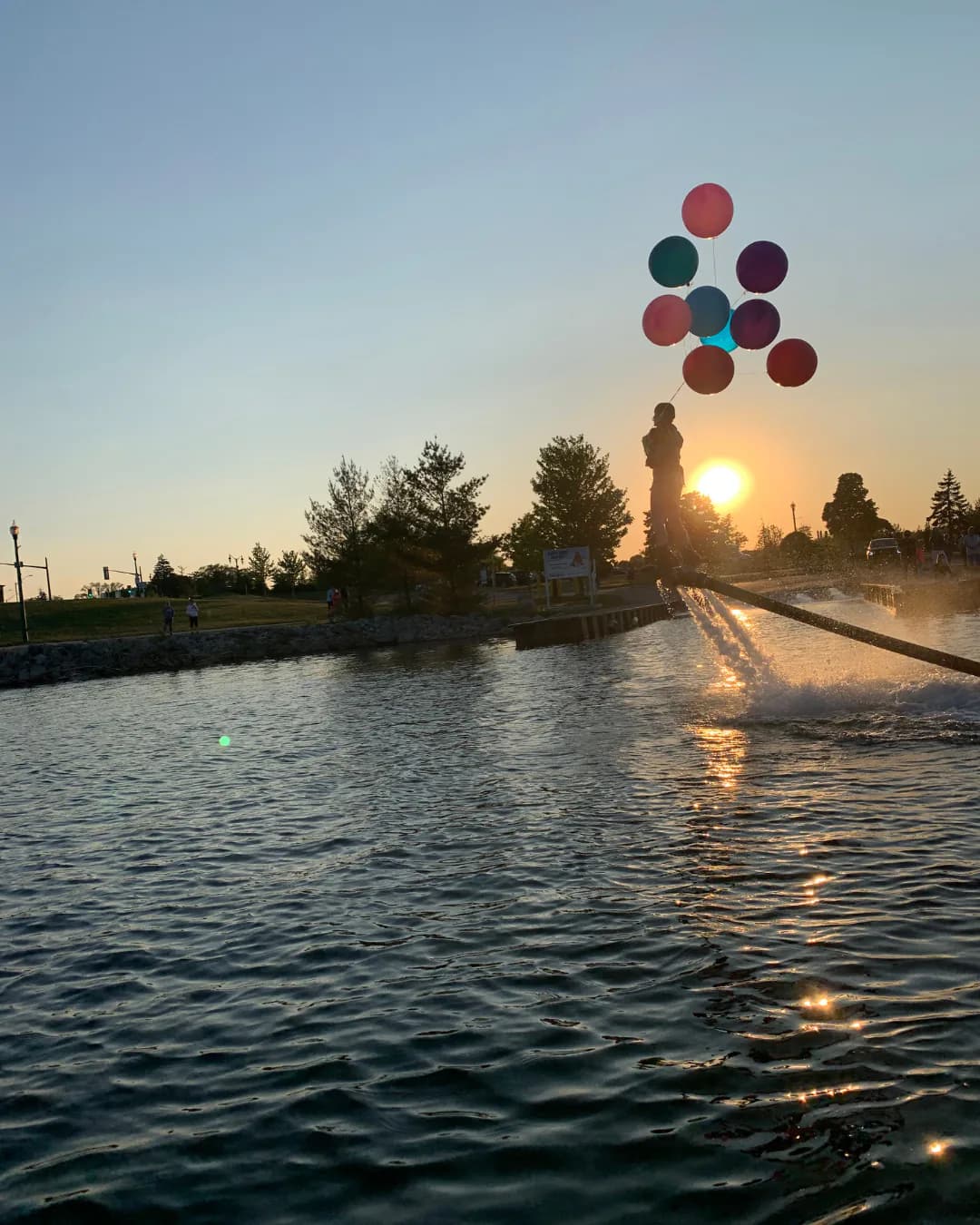 Flyboard rider carrying colourful balloons above Lake Simcoe at sunset