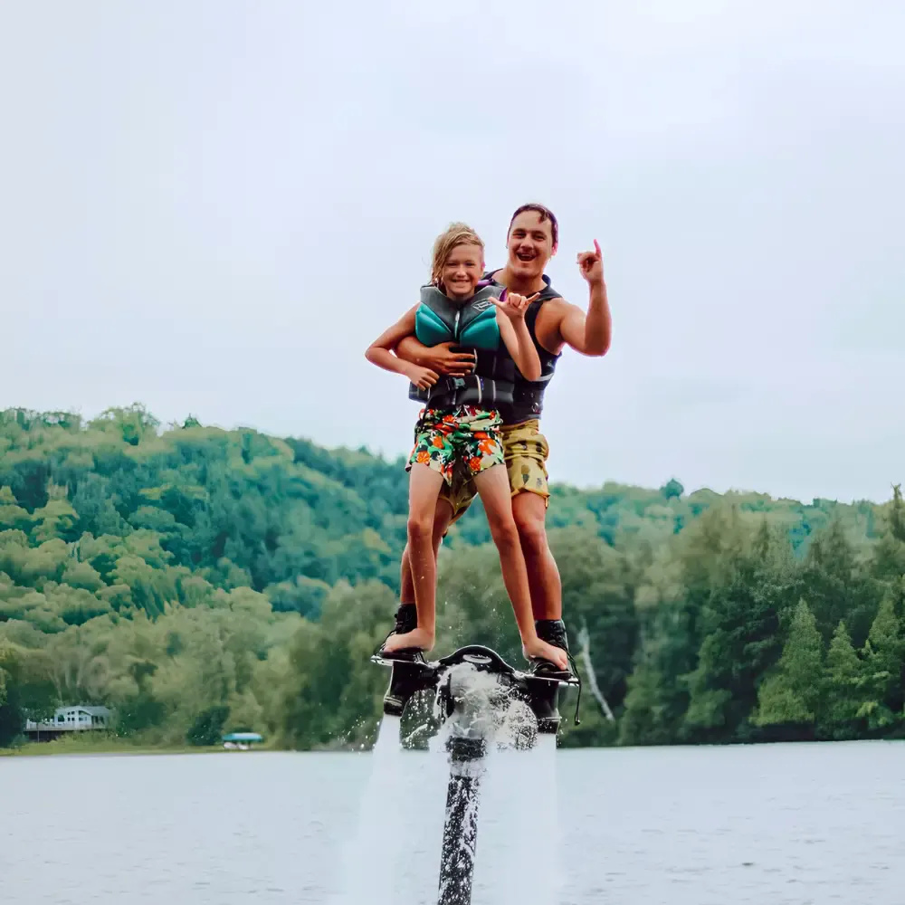 Adult and child smiling together on a Flyboard above a lake