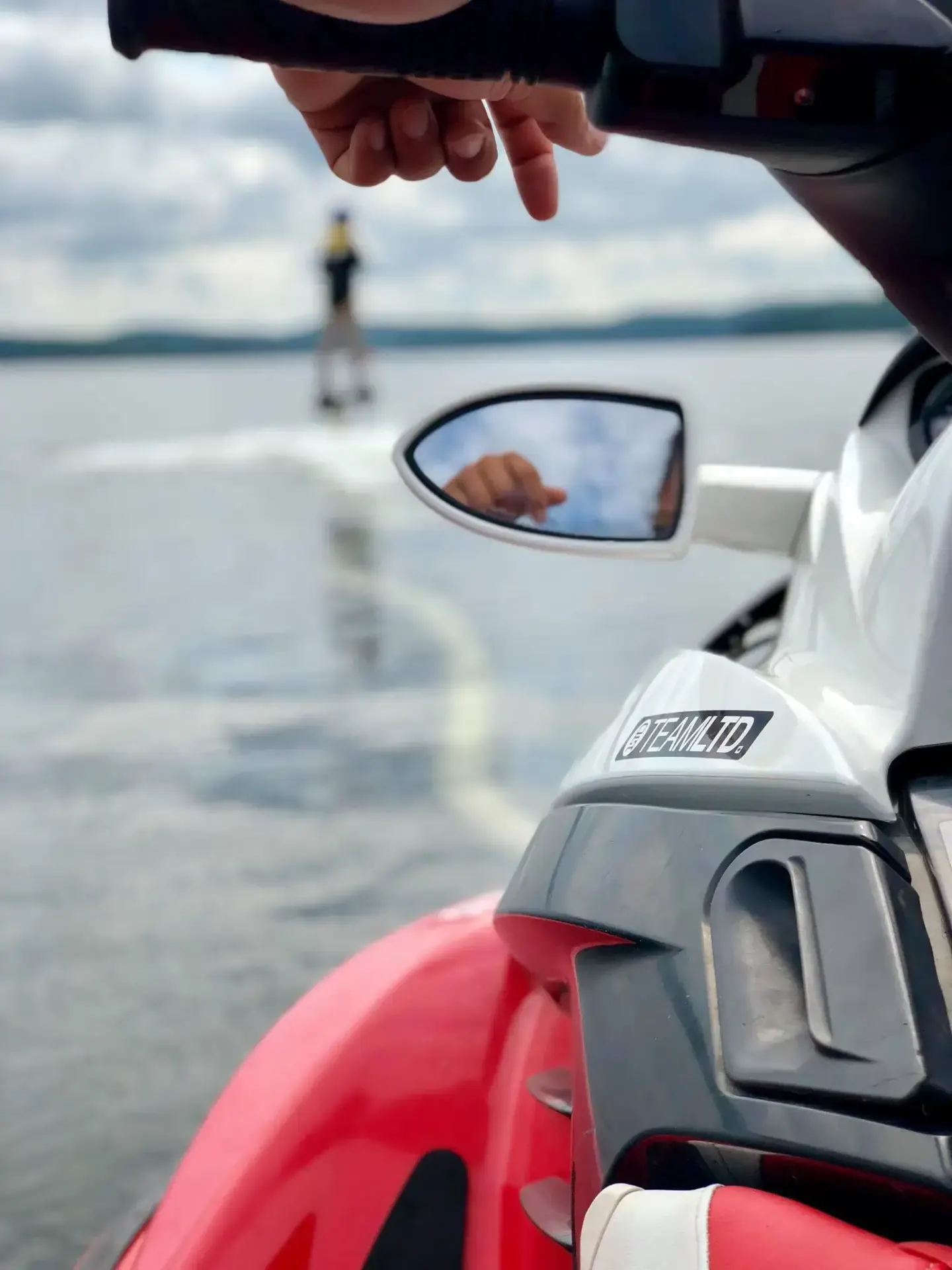 Close view of an instructor’s hand on Sea-Doo controls with a Flyboard rider blurred over the water