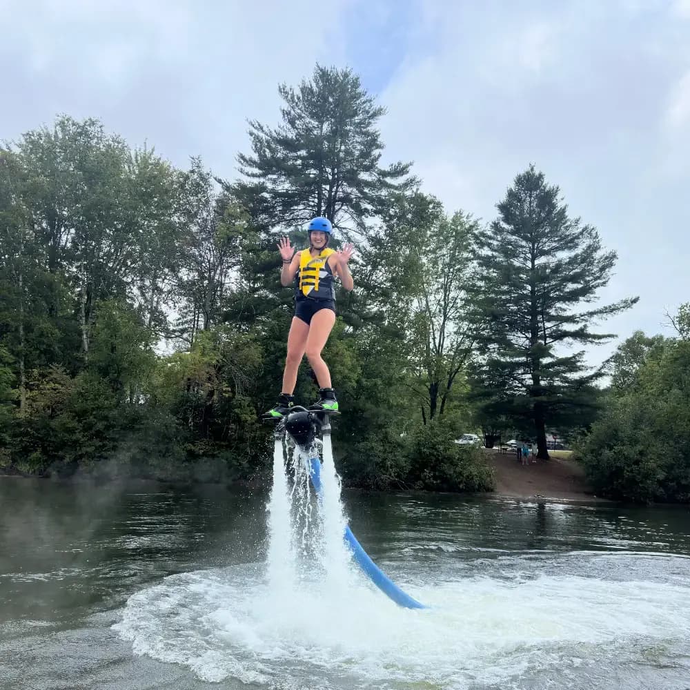 Helmeted beginner balancing on a Flyboard above the water