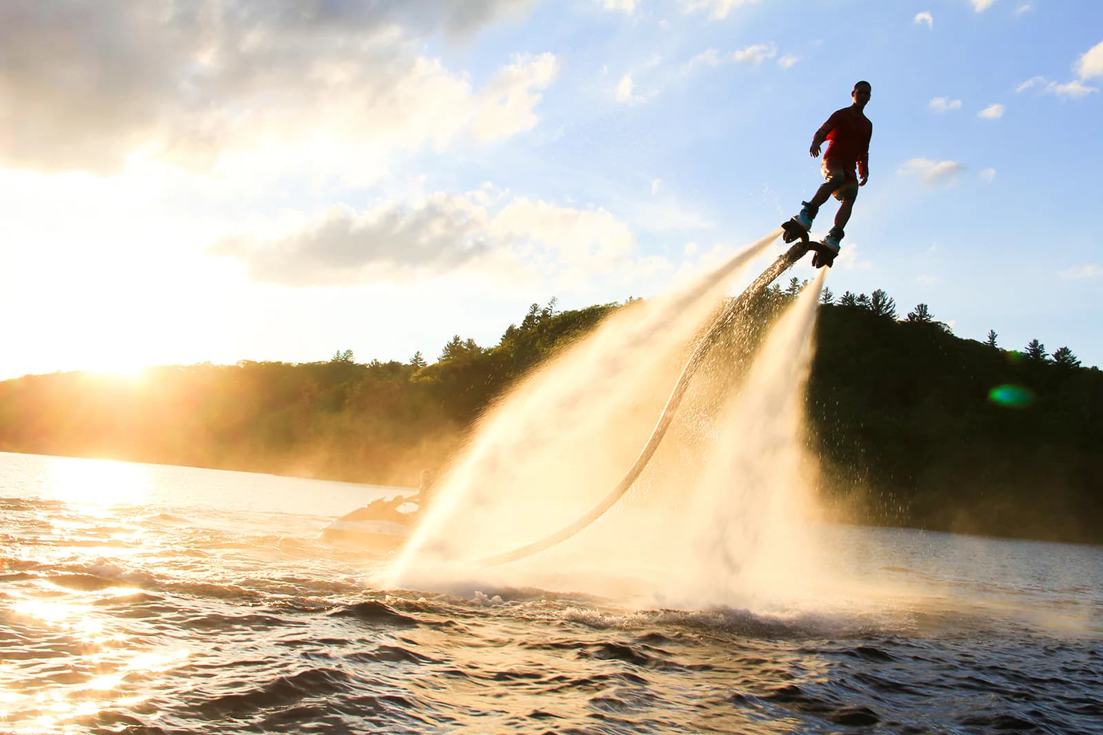 Flyboard rider flying above a forested lake in golden evening light