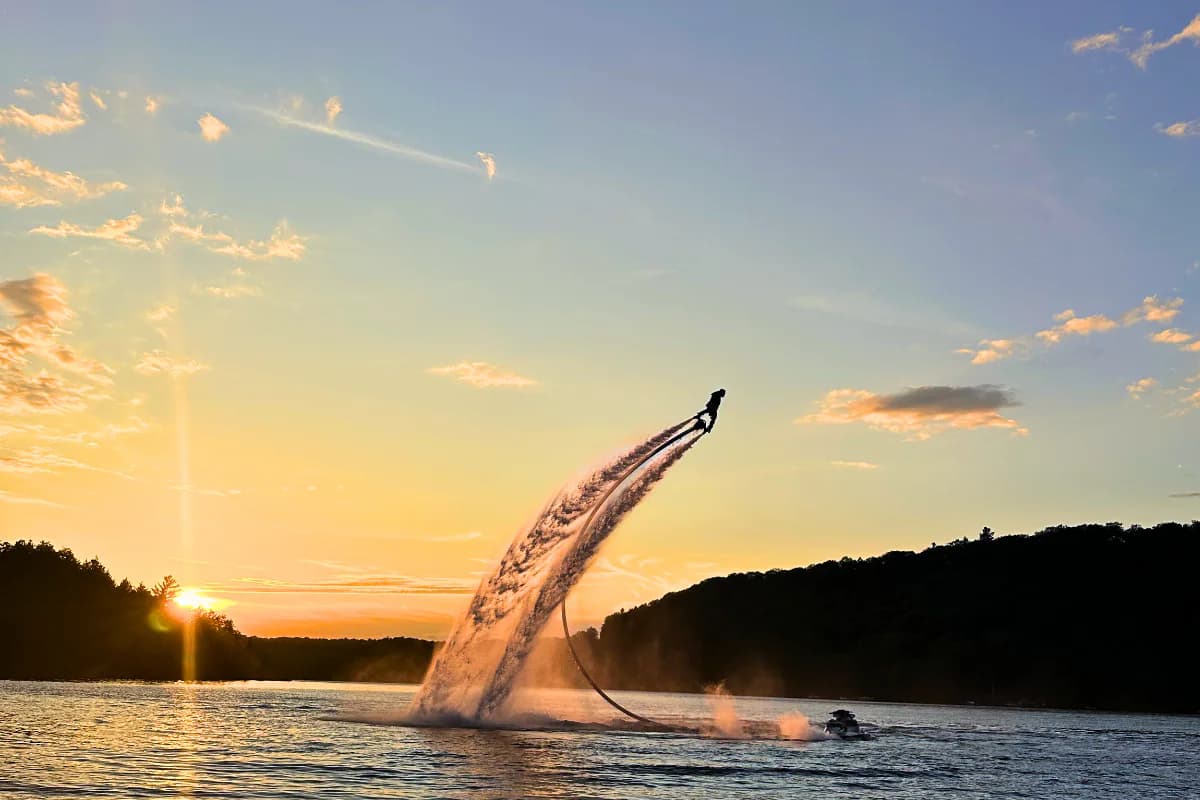 Flyboard rider soaring above a lake at sunset with a Sea-Doo below