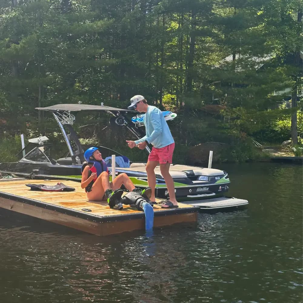 Instructor coaching a helmeted participant seated beside Flyboard equipment on a cottage dock